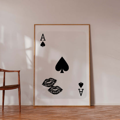 Framed artwork with playing card symbols on a wall next to a chair and plant.
