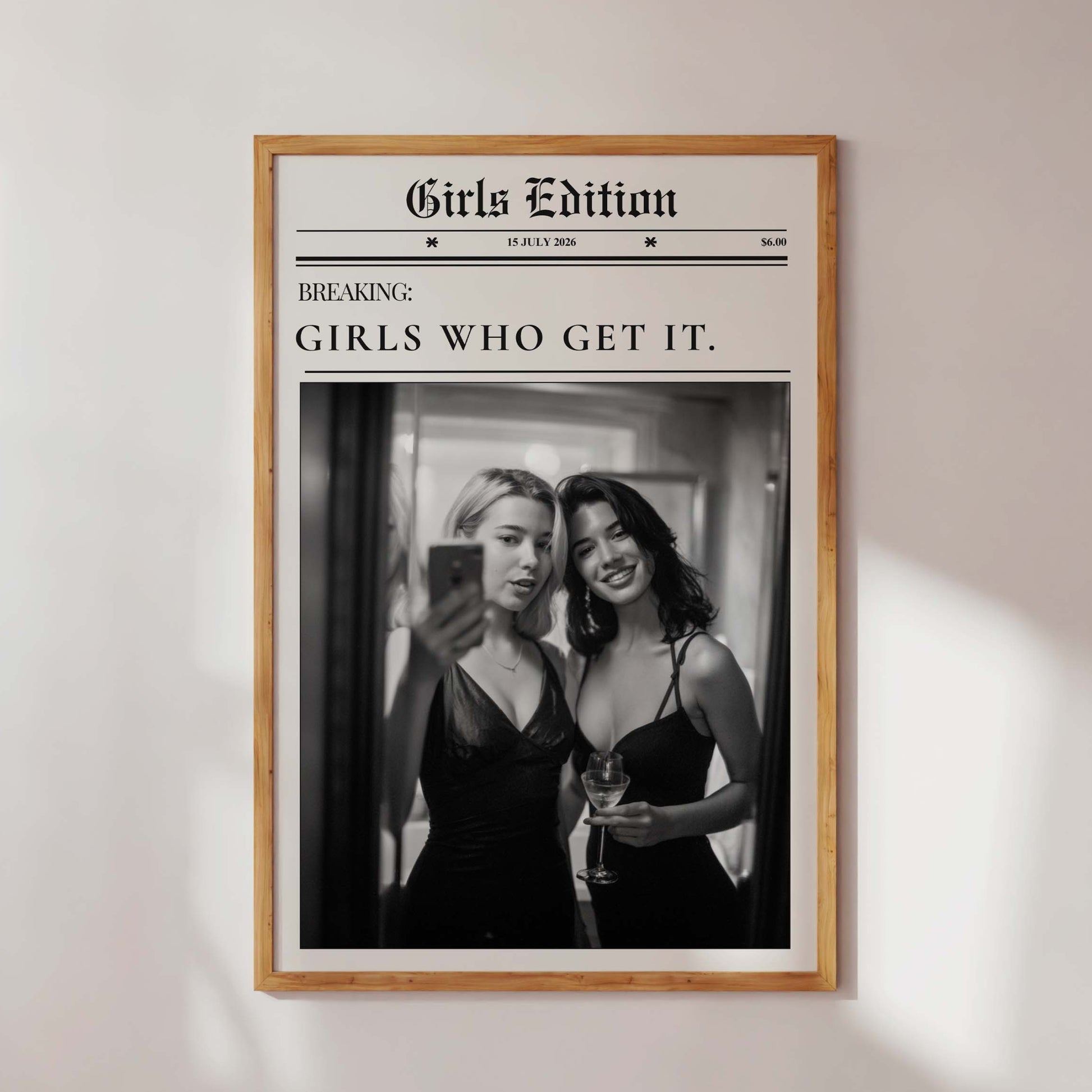 Framed poster with two women taking a selfie and text 'Girls Edition' on a white wall.
