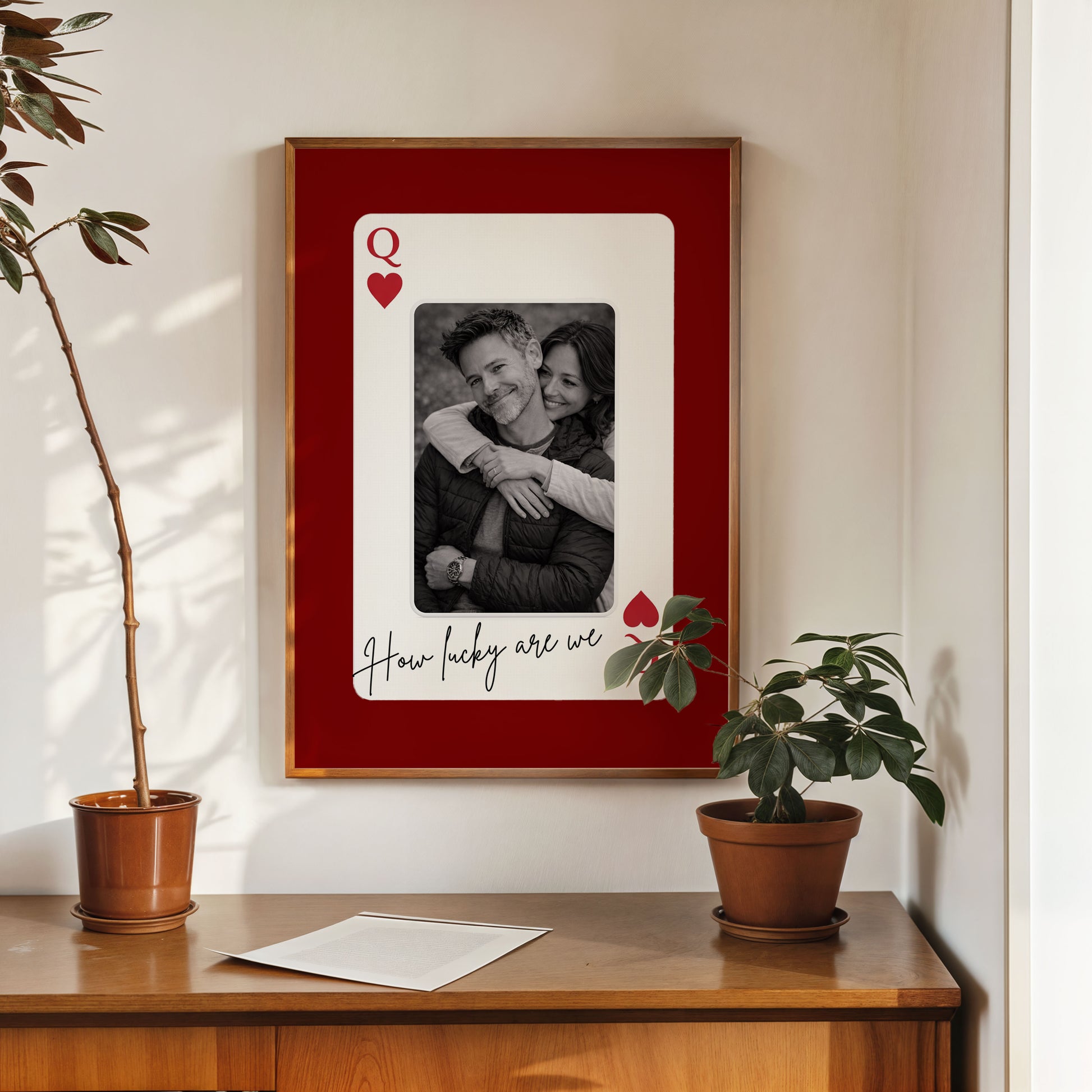Custom photo playing card wall art displayed above wooden cabinet with plants